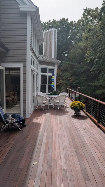 Stained deck rail with a cable railing above the trees