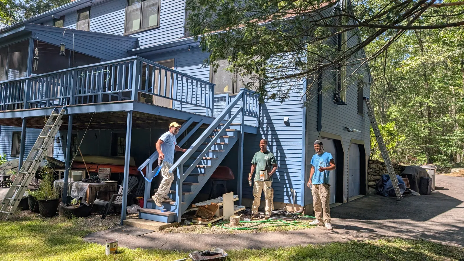 Three Beacon painters beside the stairs of a blue house they are painting, ladders up